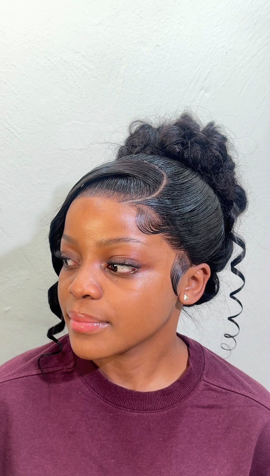 Messy updo bun with sleek laid edges and loose curled tendrils